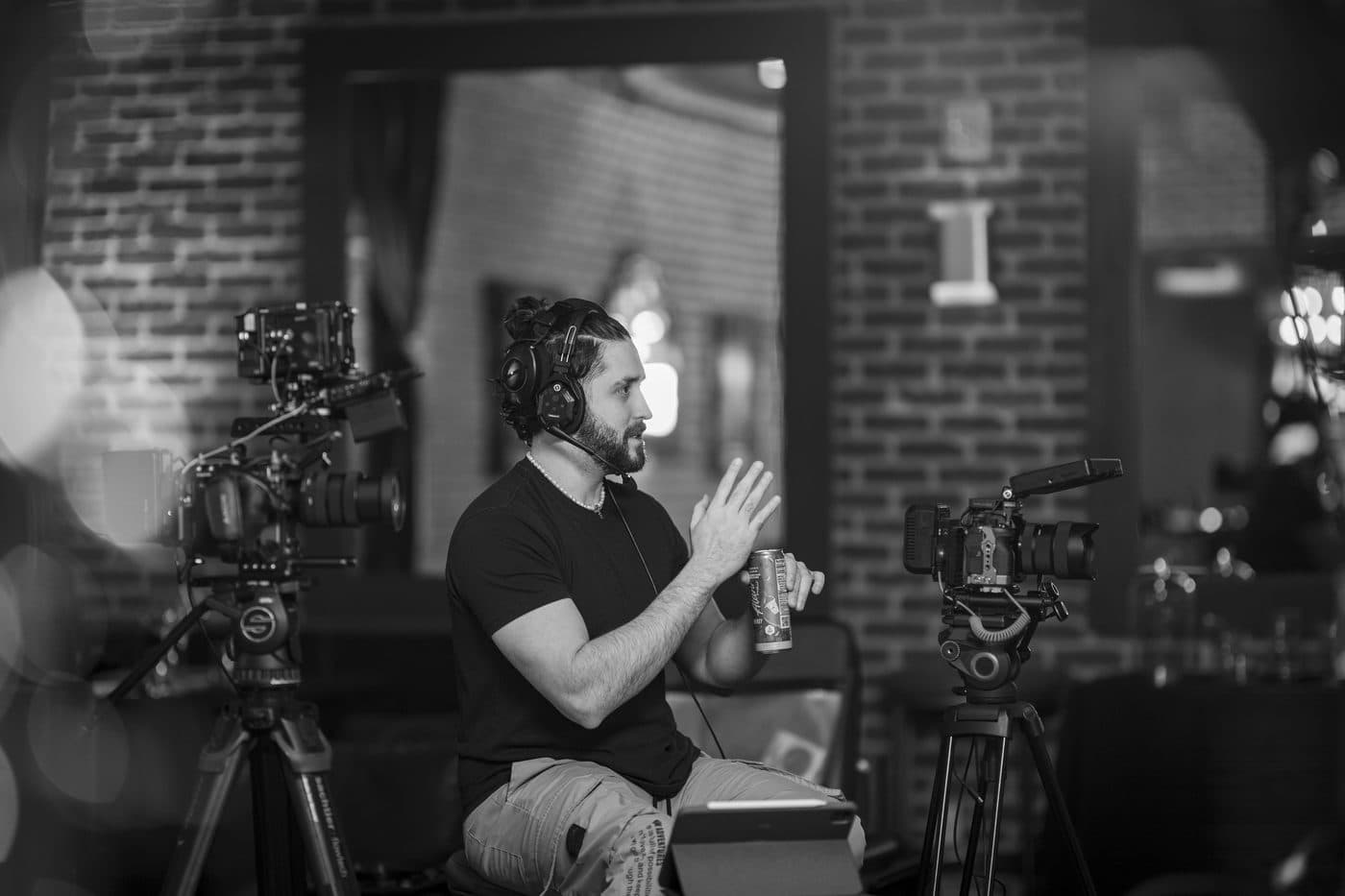 Black-and-white behind-the-scenes photo of a Hyped Visuals director gesturing while reviewing a shot on a cinema camera rig