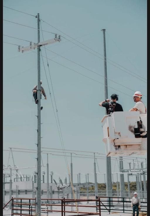 People's Electric Cooperative linemen working at a substation, with one climbing a utility pole and another in a bucket truck.
