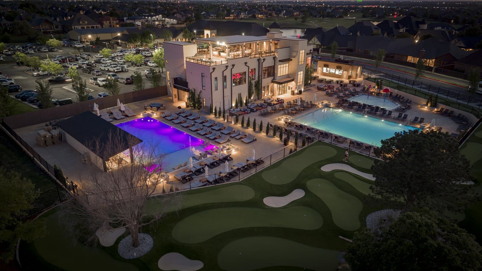 Aerial view of Rose Creek Country Club's illuminated pool deck and golf putting green at dusk, Edmond, Oklahoma